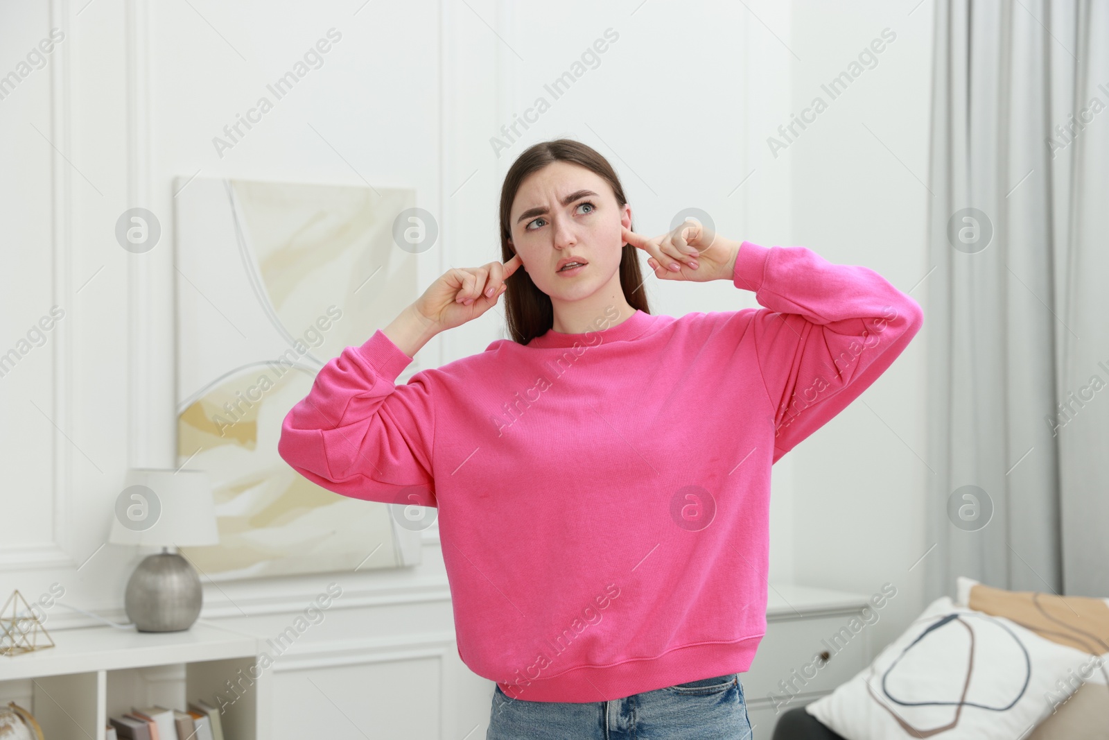 Photo of Annoyed woman covering her ears from loud noise at home