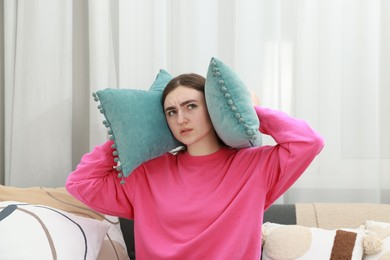 Photo of Annoyed woman covering her ears with pillows from loud noise at home