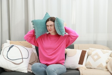 Photo of Annoyed woman covering her ears with pillows from loud noise at home