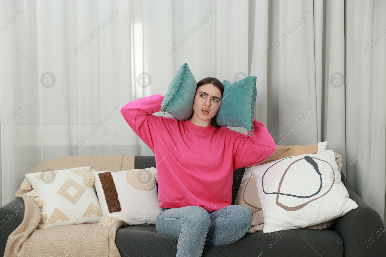 Photo of Annoyed woman covering her ears with pillows from loud noise at home