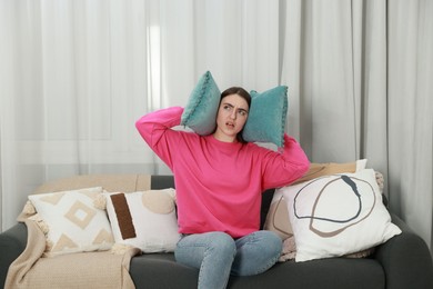 Photo of Annoyed woman covering her ears with pillows from loud noise at home