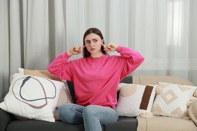 Photo of Annoyed woman covering her ears from loud noise at home