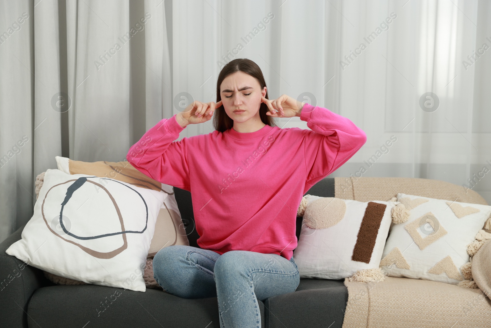 Photo of Annoyed woman covering her ears from loud noise at home