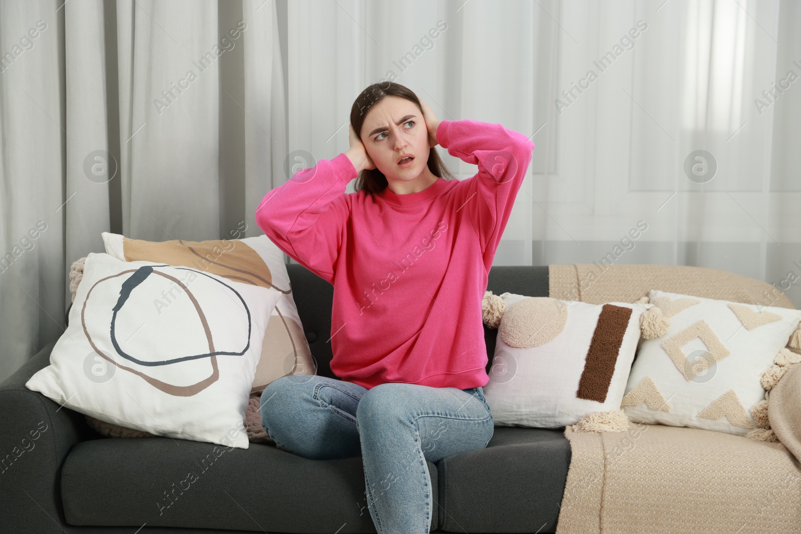 Photo of Annoyed woman covering her ears from loud noise at home