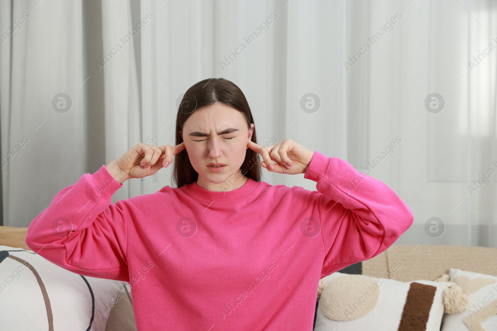 Photo of Annoyed woman covering her ears from loud noise at home