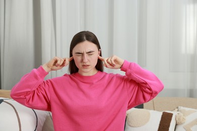 Photo of Annoyed woman covering her ears from loud noise at home