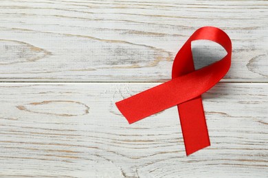 Photo of Red awareness ribbon on wooden background, top view. Space for text