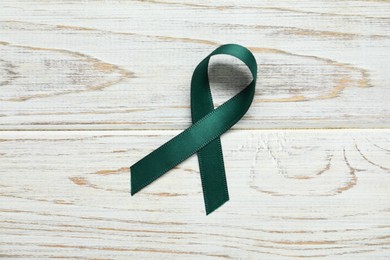 Photo of Green awareness ribbon on wooden background, top view