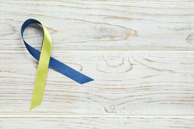 Photo of Yellow and blue awareness ribbon on wooden background, top view. Space for text