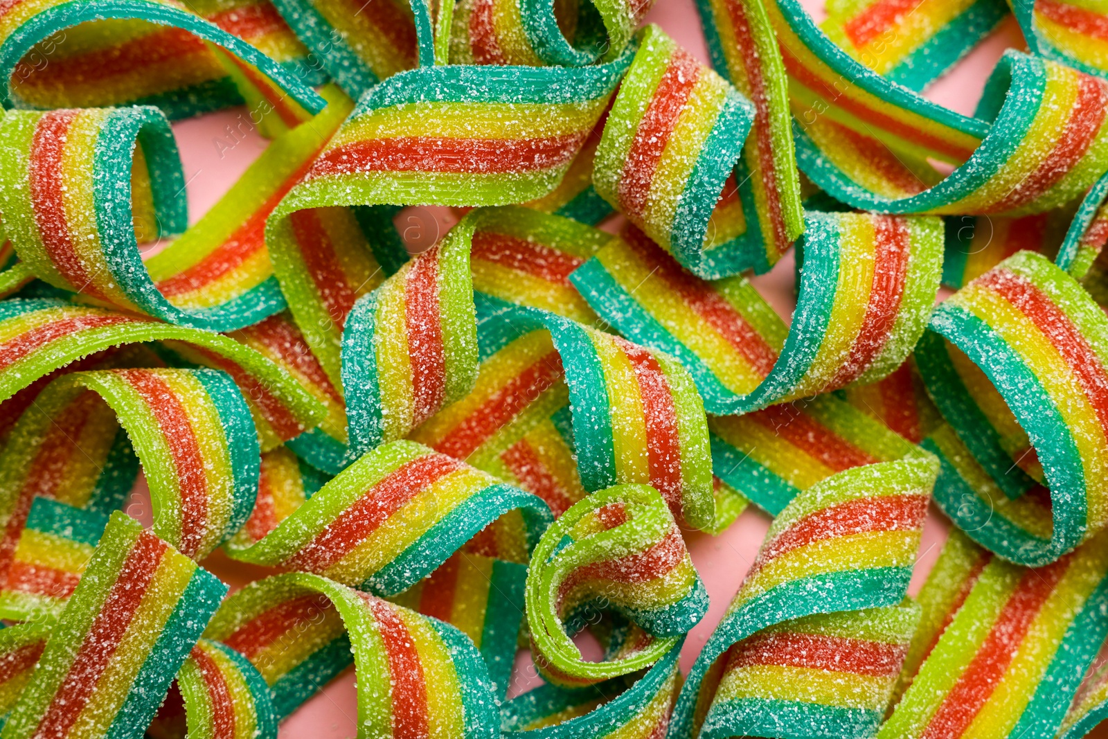 Photo of Tasty rainbow sour belts on pink background, top view