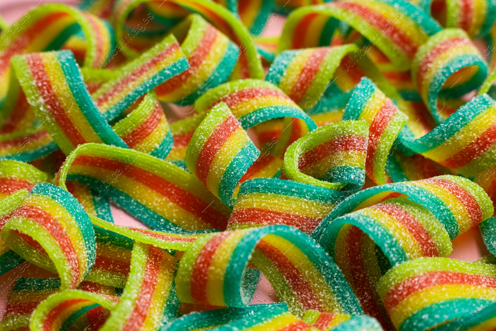 Photo of Tasty rainbow sour belts on pink background, closeup