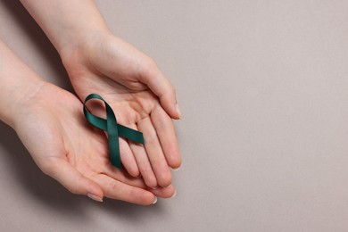 Photo of Woman with teal ribbon on grey background, top view with space for text. Ovarian cancer and gynecological disorders awareness