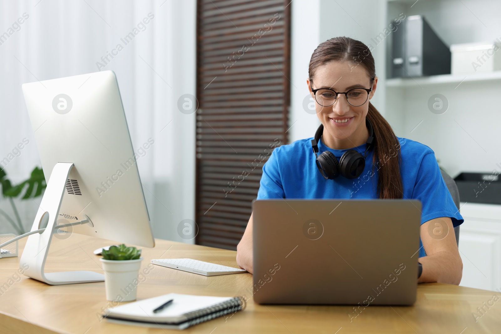 Photo of Programmer working on laptop and computer at wooden desk indoors