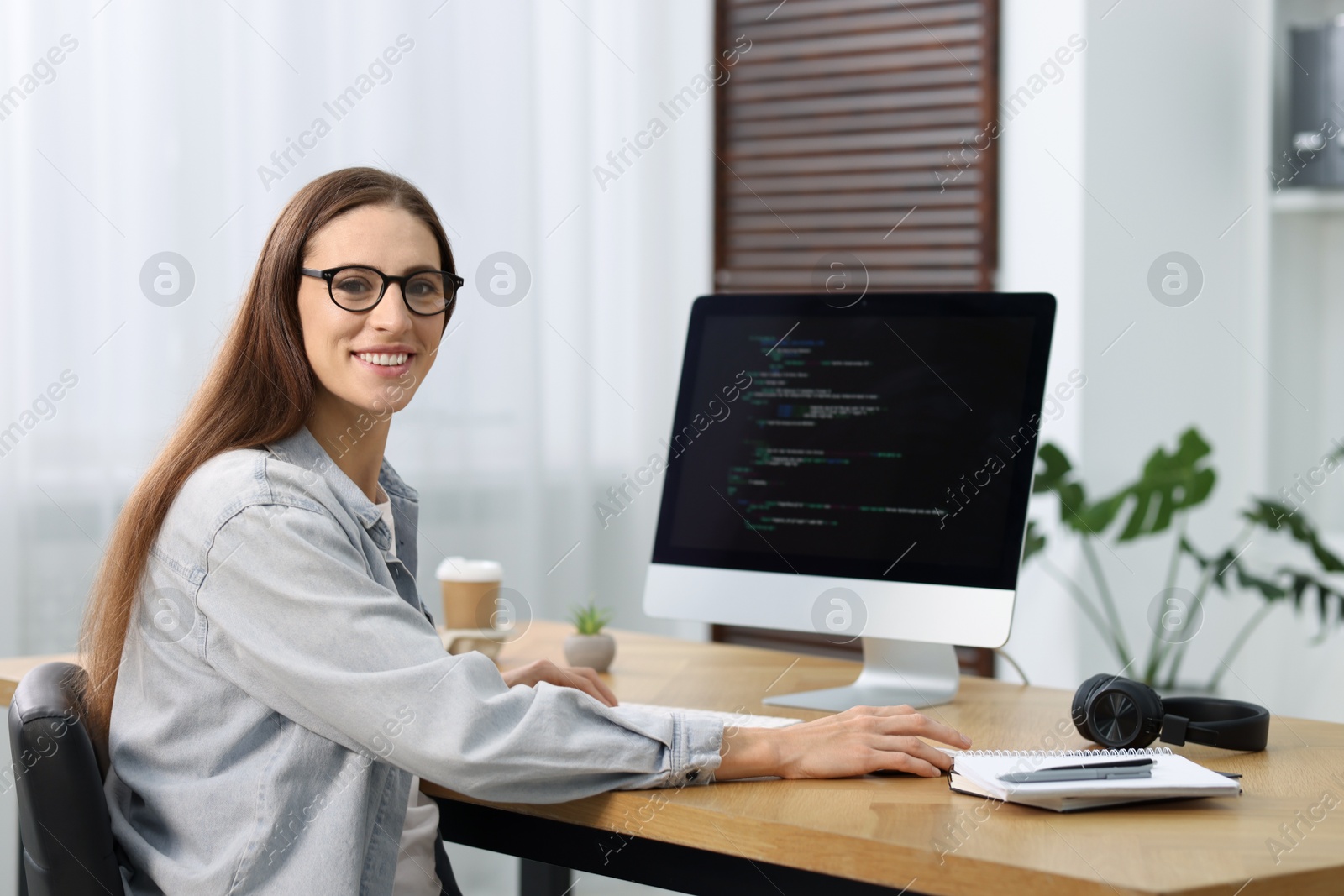 Photo of Programmer working on computer at wooden desk indoors