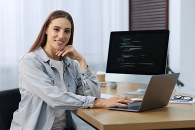 Photo of Programmer working on laptop and computer at wooden desk indoors