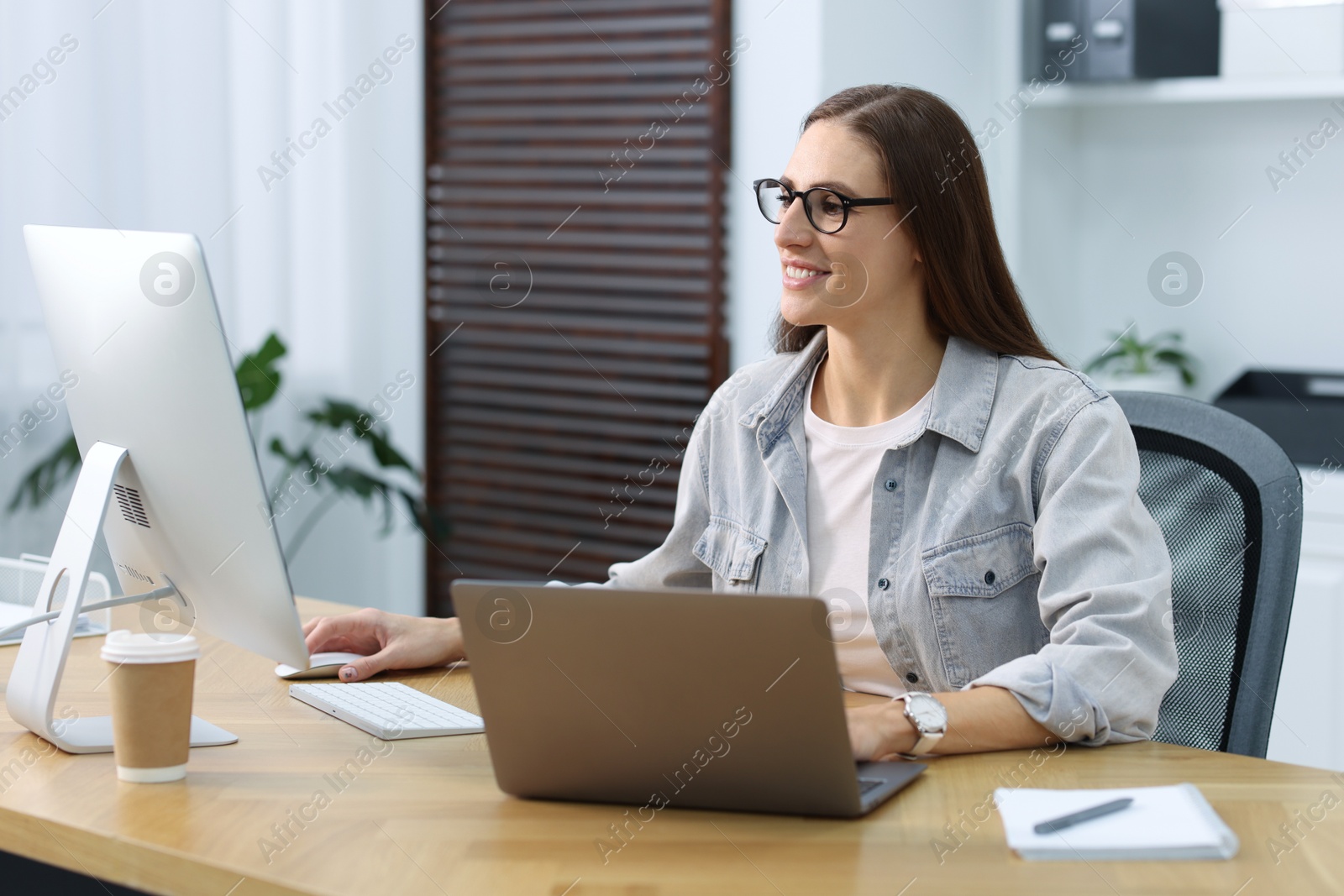 Photo of Programmer working on laptop and computer at wooden desk indoors