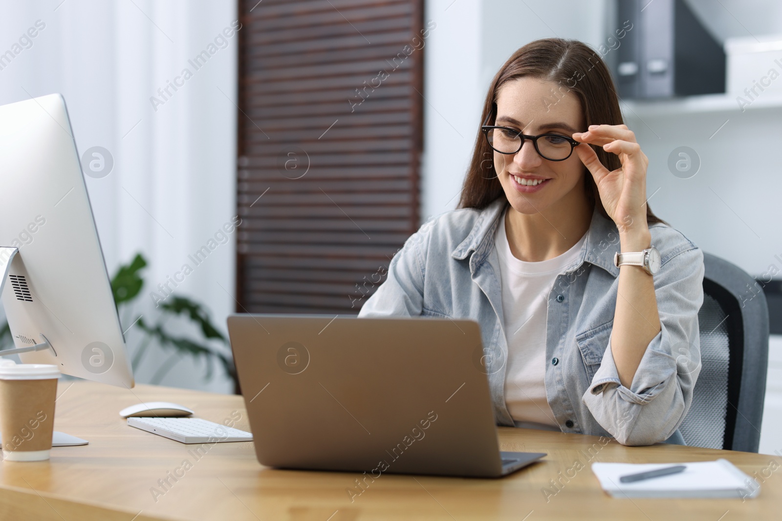 Photo of Programmer working on laptop and computer at wooden desk indoors