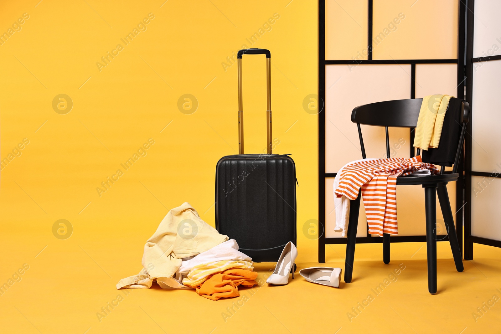 Suitcase with messy pile of clothes and chair on yellow background Photo of Suitcase with messy pile of clothes and chair on yellow background
