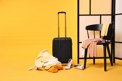 Photo of Suitcase with messy pile of clothes and chair on yellow background