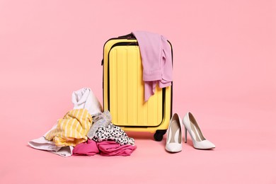 Photo of Suitcase, messy clothes and shoes on pink background