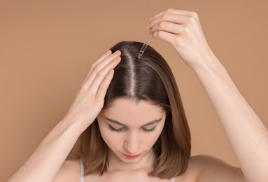 Photo of Hair loss problem. Girl applying serum onto hairline on dark beige background, closeup