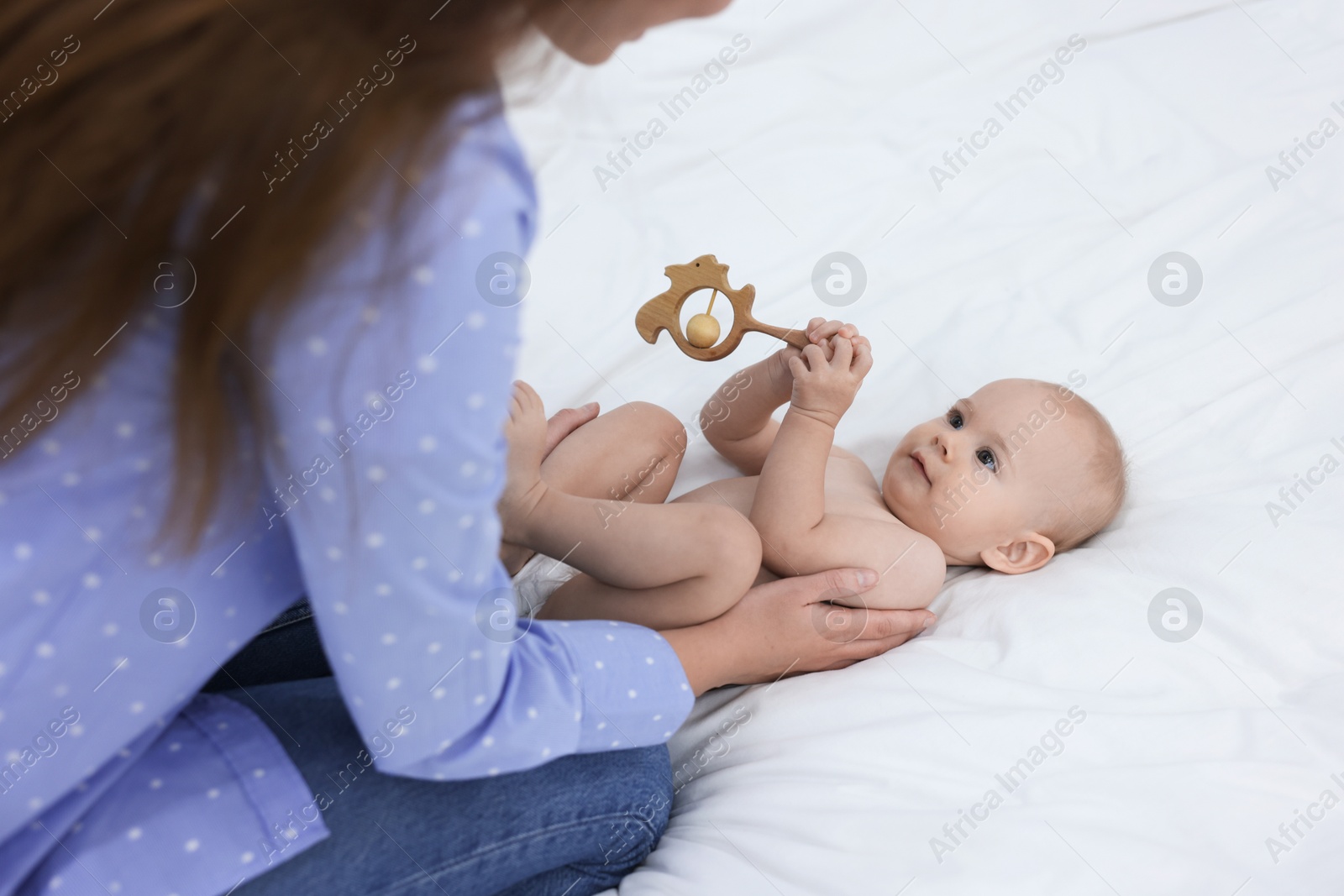 Photo of Mother and her cute little baby with rattle on bed indoors