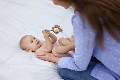 Photo of Mother and her cute little baby with rattle on bed indoors