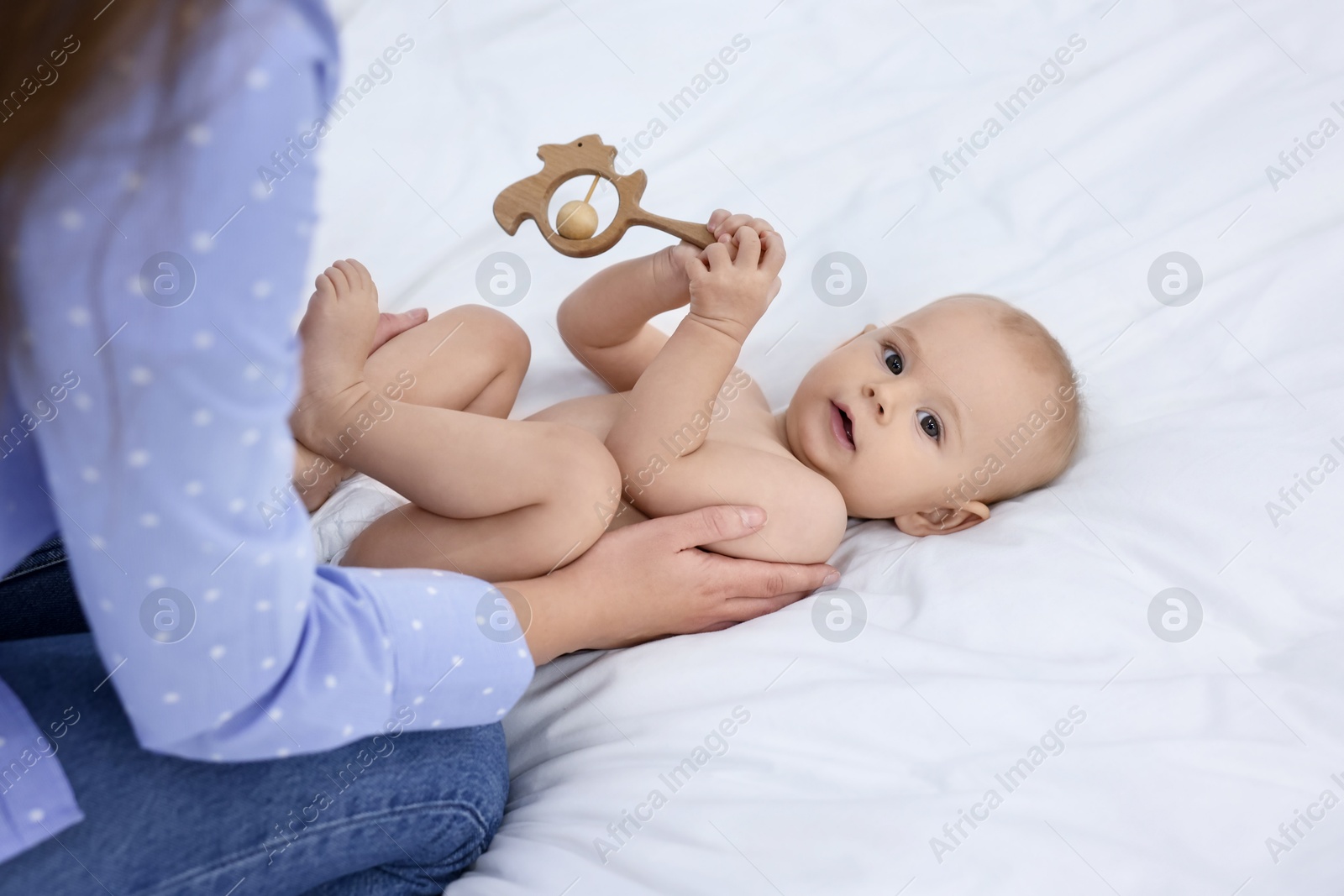 Photo of Mother and her cute little baby with rattle on bed indoors