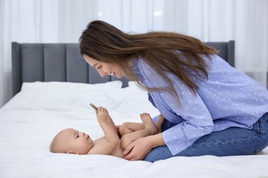 Photo of Mother and her cute little baby with rattle on bed indoors