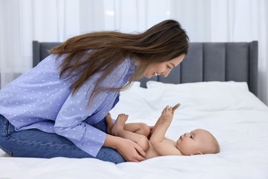 Photo of Mother and her cute little baby with rattle on bed indoors