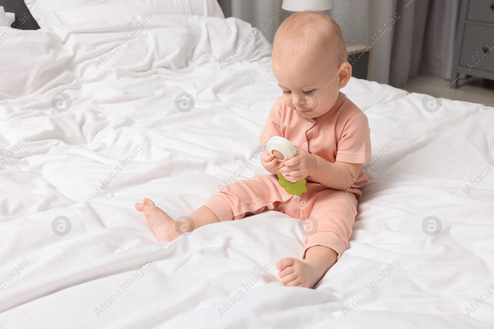 Photo of Cute little baby with rattle on bed indoors