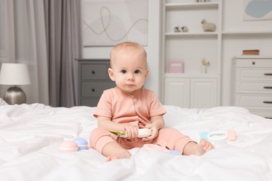 Photo of Cute little baby with rattles on bed indoors