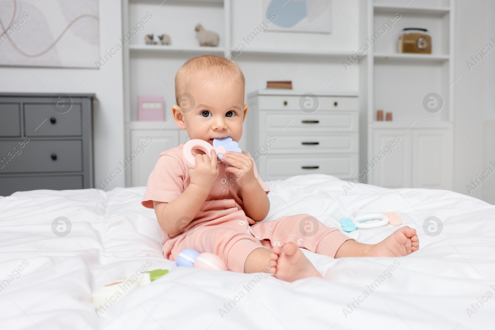 Photo of Cute little baby with rattles on bed indoors