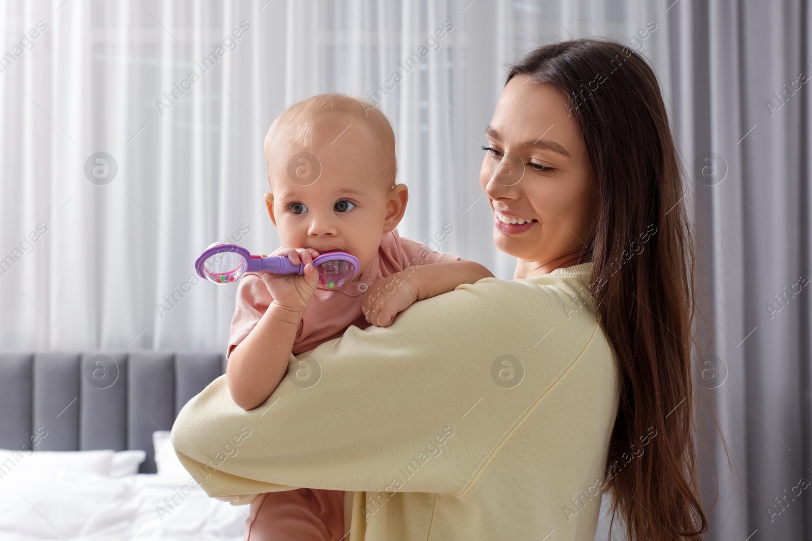 Photo of Mother and her cute little baby with rattle at home