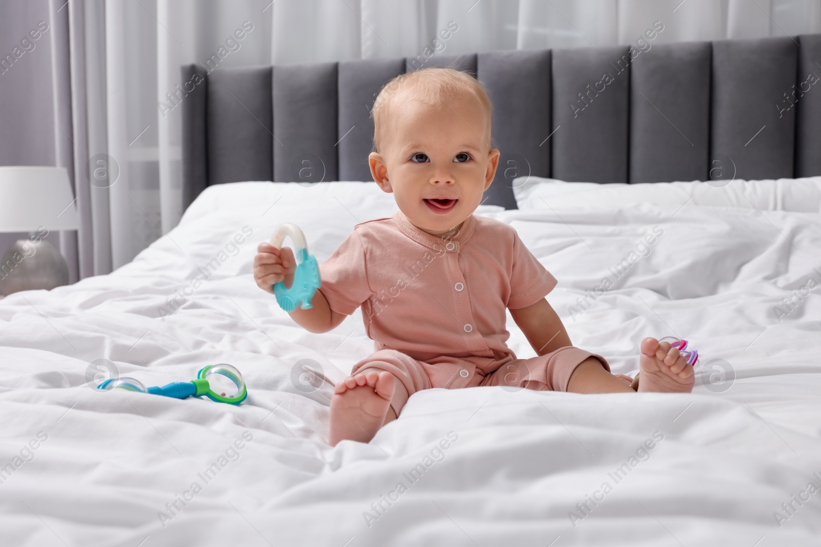 Photo of Cute little baby with rattles on bed indoors