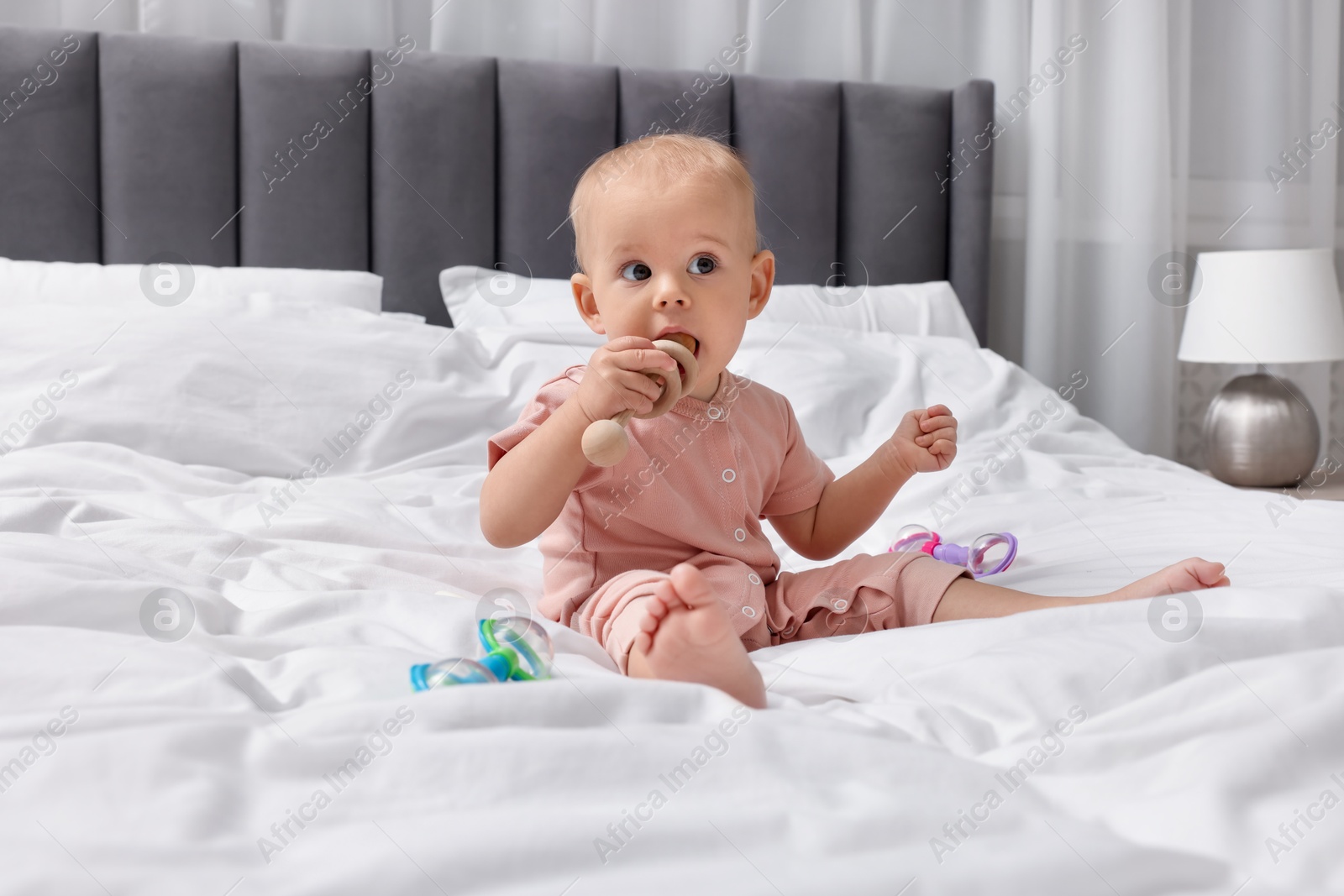 Photo of Cute little baby with rattles on bed indoors