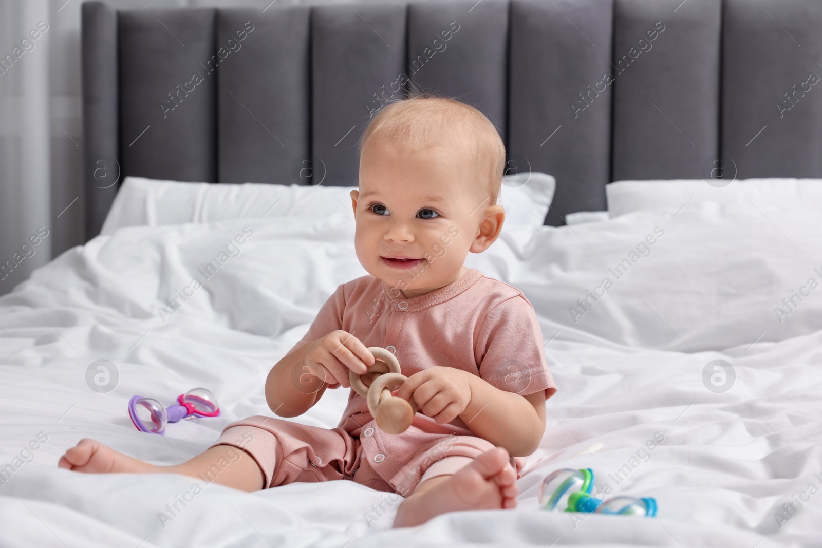 Photo of Cute little baby with rattles on bed indoors