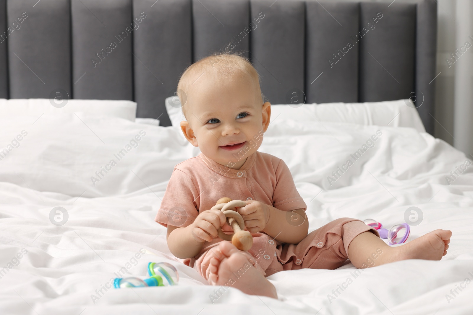 Photo of Cute little baby with rattles on bed indoors