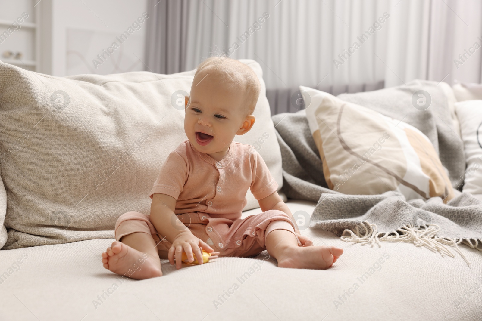 Photo of Cute little baby with rattle on sofa indoors