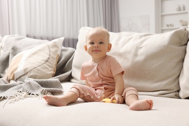 Photo of Cute little baby with rattle on sofa indoors