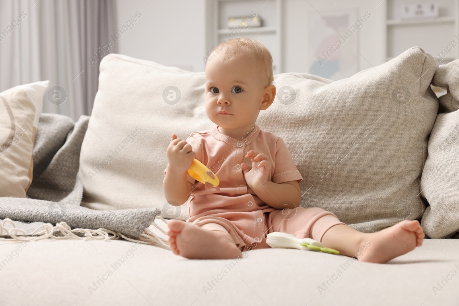 Photo of Cute little baby with rattle on sofa indoors