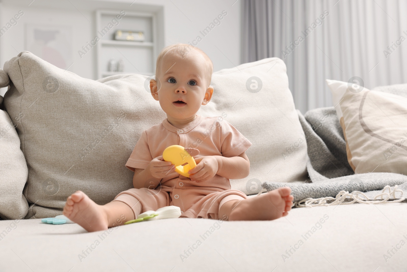 Photo of Cute little baby with rattle on sofa indoors