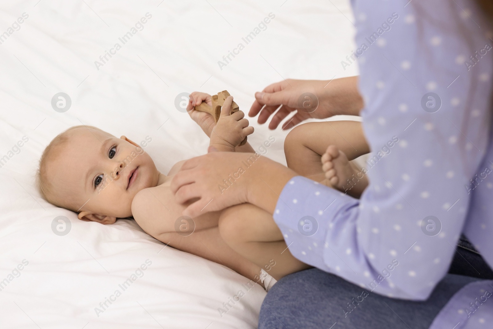 Photo of Mother and her cute little baby with rattle on bed indoors, closeup