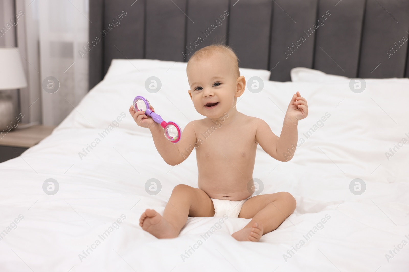 Photo of Cute little baby with rattle on bed indoors