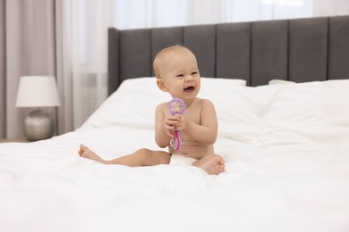 Photo of Cute little baby with rattle on bed indoors