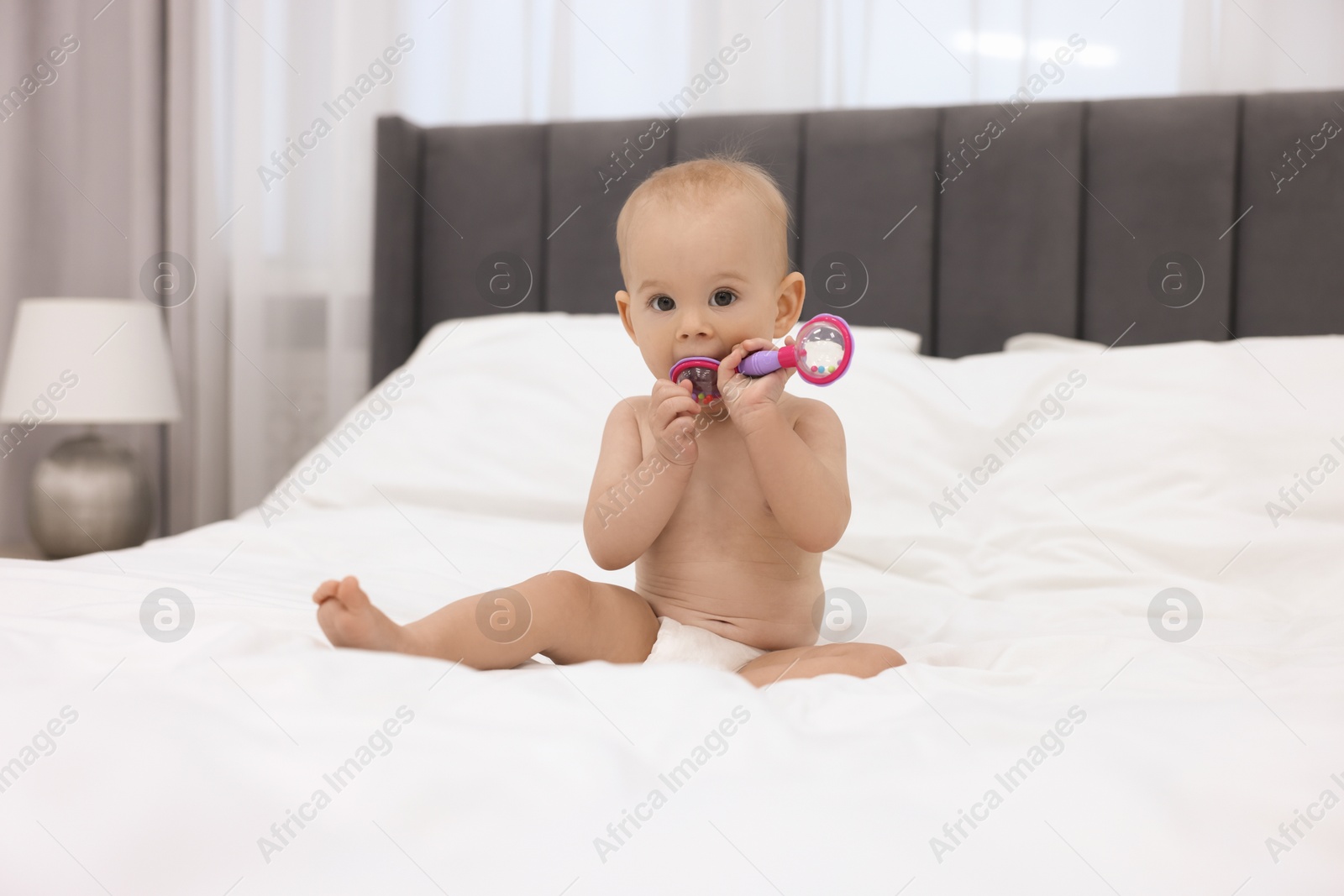 Photo of Cute little baby with rattle on bed indoors