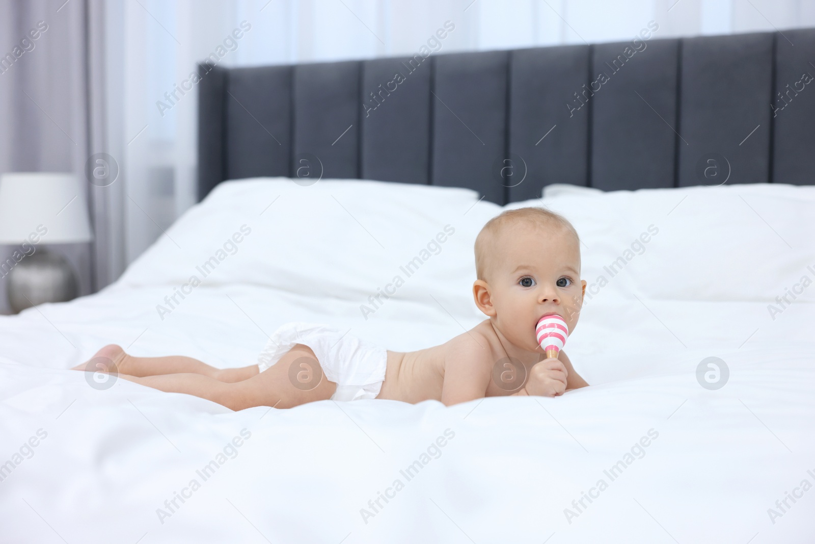 Photo of Cute little baby with rattle on bed indoors