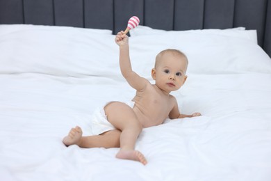 Photo of Cute little baby with rattle on bed indoors