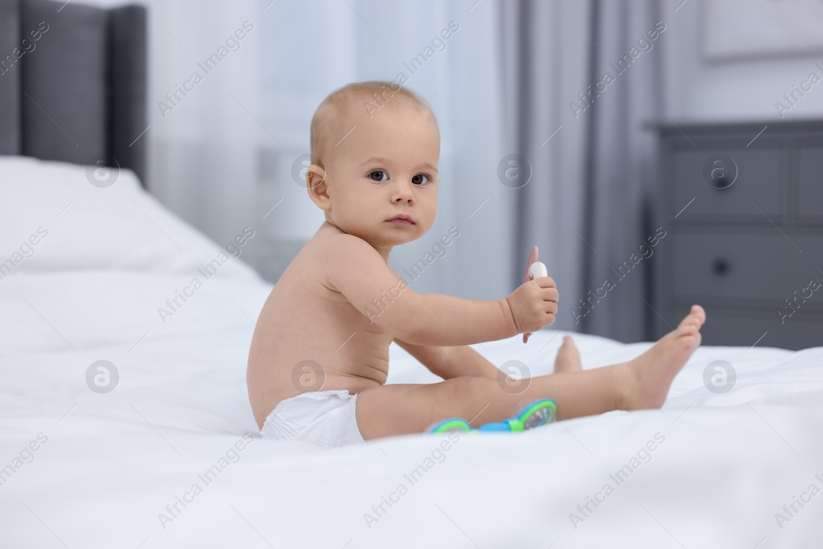 Photo of Cute little baby with rattles on bed indoors