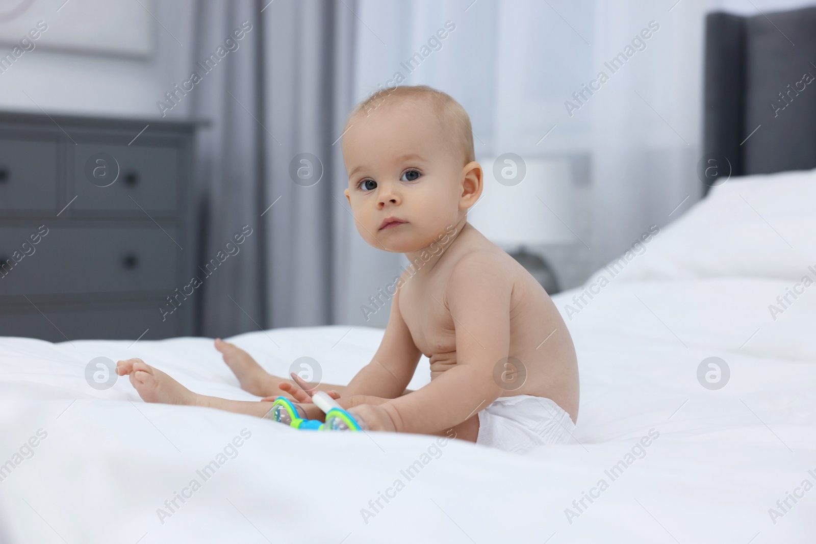 Photo of Cute little baby with rattles on bed indoors